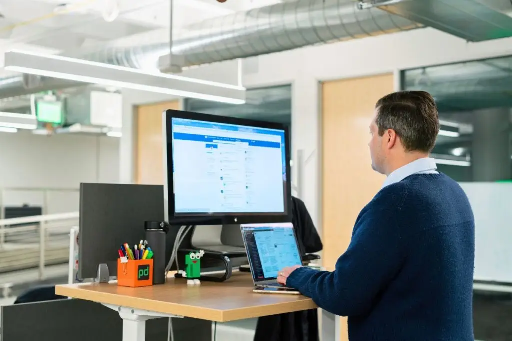 Professional working at a standing desk using a computer and laptop